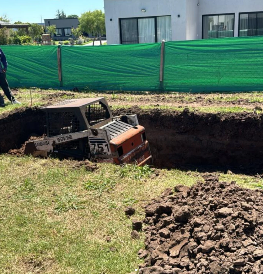Minicargadora trabajando en una excavación junto a una vivienda
